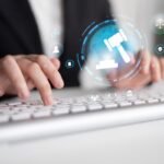 Mãos digitando em teclado com ícones de justiça e tecnologia.